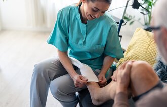 Bildet viser en sykepleier som hjelper en mann med å ta på kompresjonsstrømper