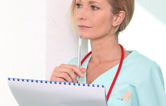 En kvinnelig sykepleier står og tenker med en penn og skriveblokk