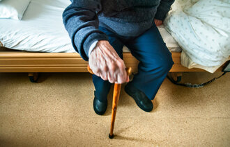 Bildet viser hånden til en gammel mann som støtter seg til en stokk.