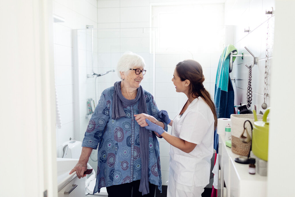 Bildet viser en hjemmesykepleier som smiler til og prater med en pasient