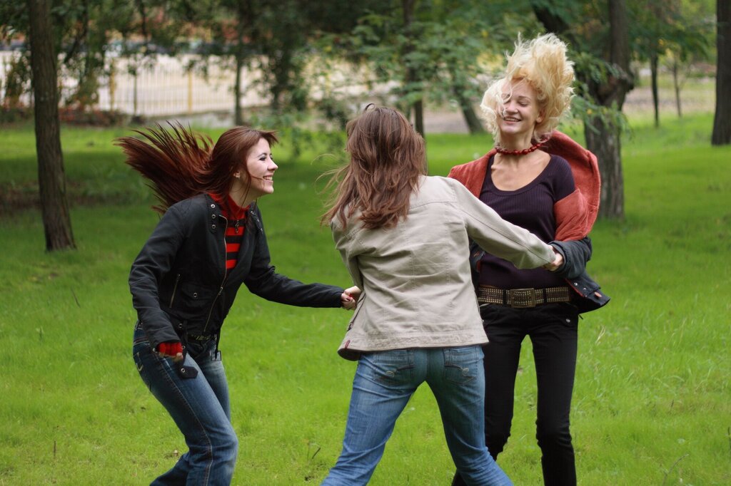 Tre kvinner danser i ring ute i en park