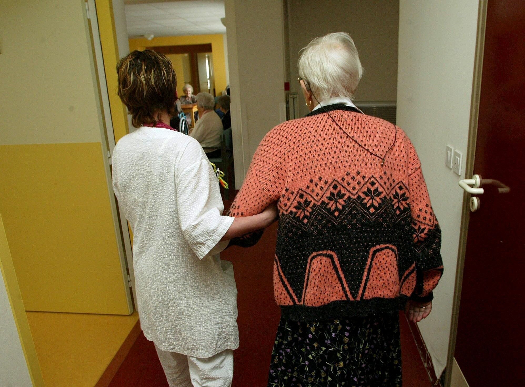 På sykehjem En pleier leier en sykehjemspasient mot spisestuen. Bildet er tatt bakfra.