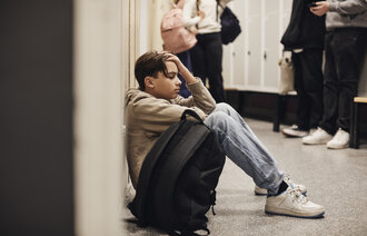 Bildet viser en bedrøvet, ung gutt som sitter på gulvet i en skolekorridor