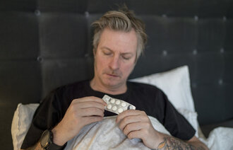 Bildet viser en mann i senga med tabletter.