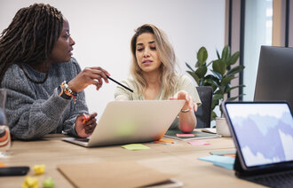 Helsesykepleier og skoleansatt diskuterer Bildet viser to kvinner som sitter og diskuterer foran en PC