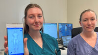 Bildet viser to sykepleiere som viser frem en mobilapp.